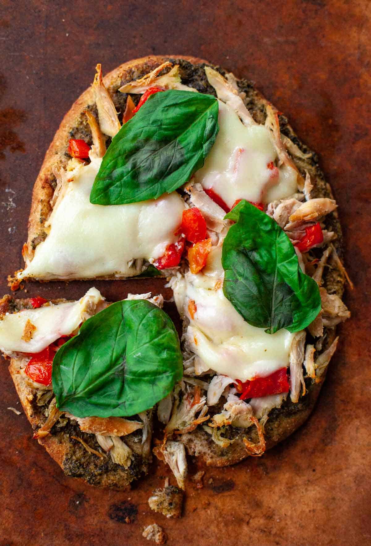 chicken pesto flatbread with mozzarella tomatoes basil on pizza stone with one slice cut 