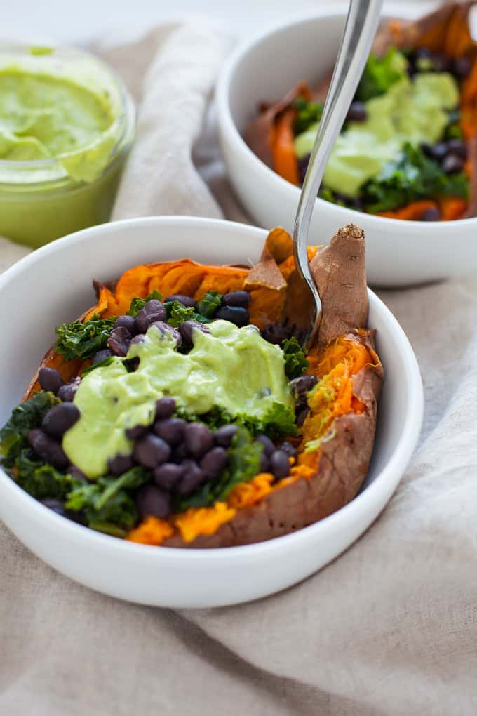 two white bowls with loaded sweet potato, kale, beans, and green goddess dressing