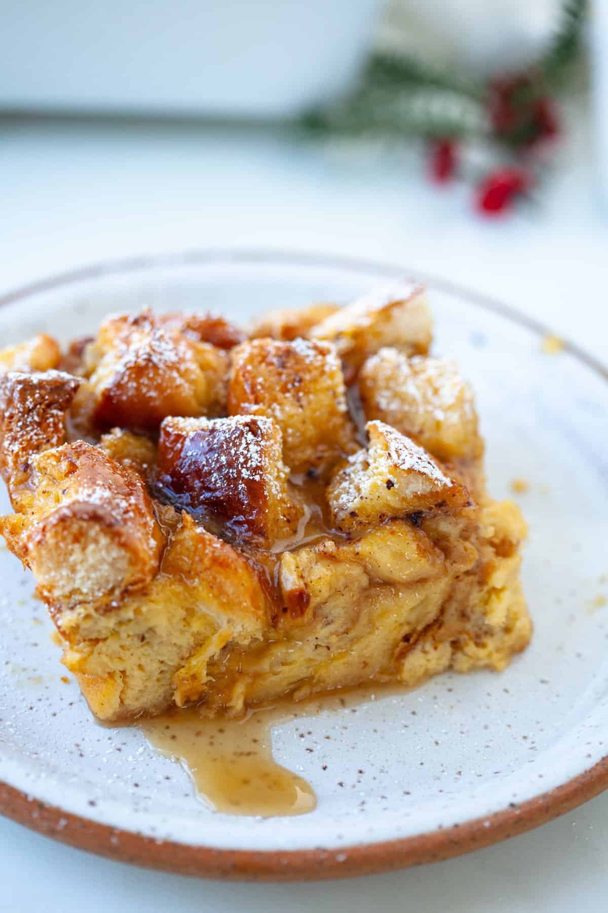 close up shot of eggnog bread pudding on white speckled plate and green foliage in background