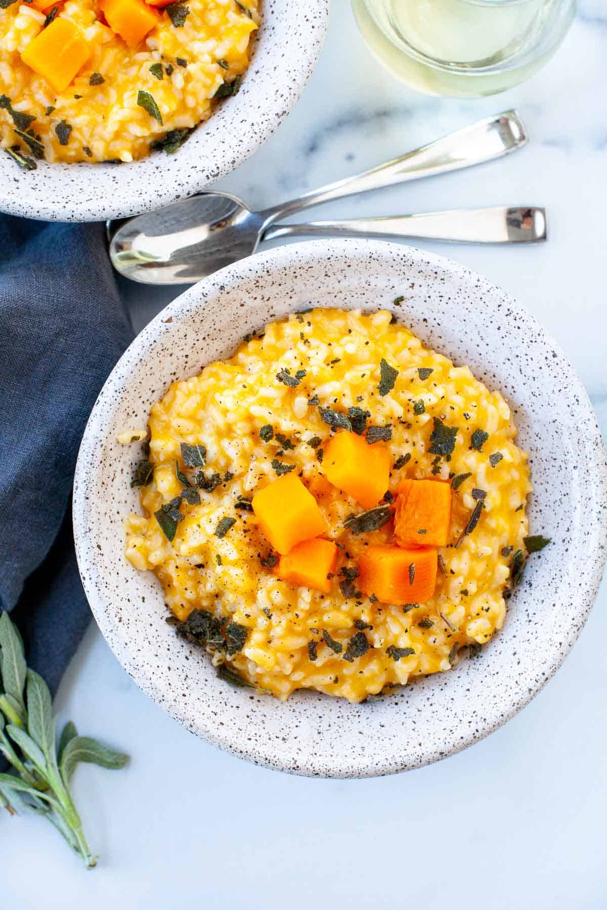 two bowls of risotto with crumbled sage and butternut squash on top with two spoons