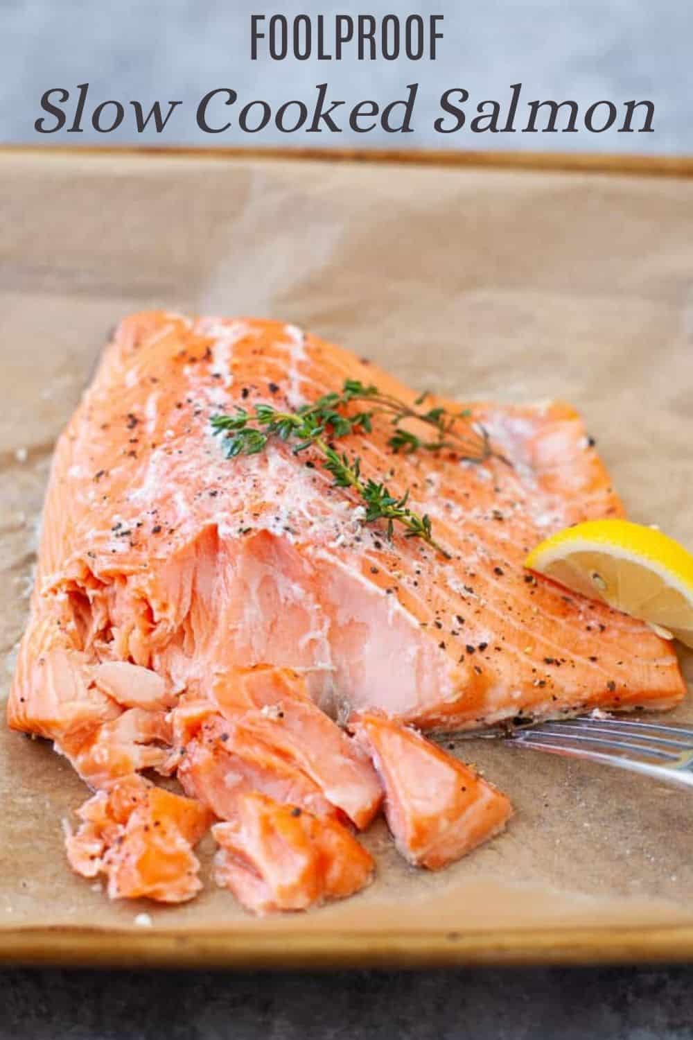 salmon on parchment paper lined baking sheet with thyme, pepper, lemon and a fork