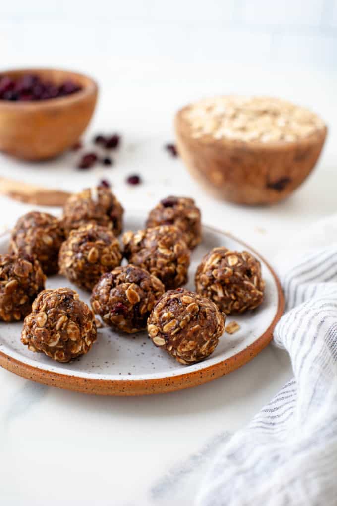 Almond Butter Protein Bites are shown on a white and orange plate with rolled oats and dried cranberries in the background