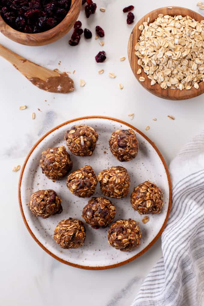 Almond butter protein bites on a white plate beside bowls of rolled oats and almond butter