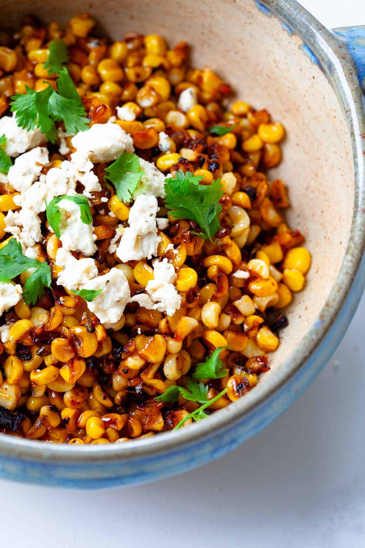 close up image of blackened corn garnished with cilantro and feta cheese in bowl with blue rim