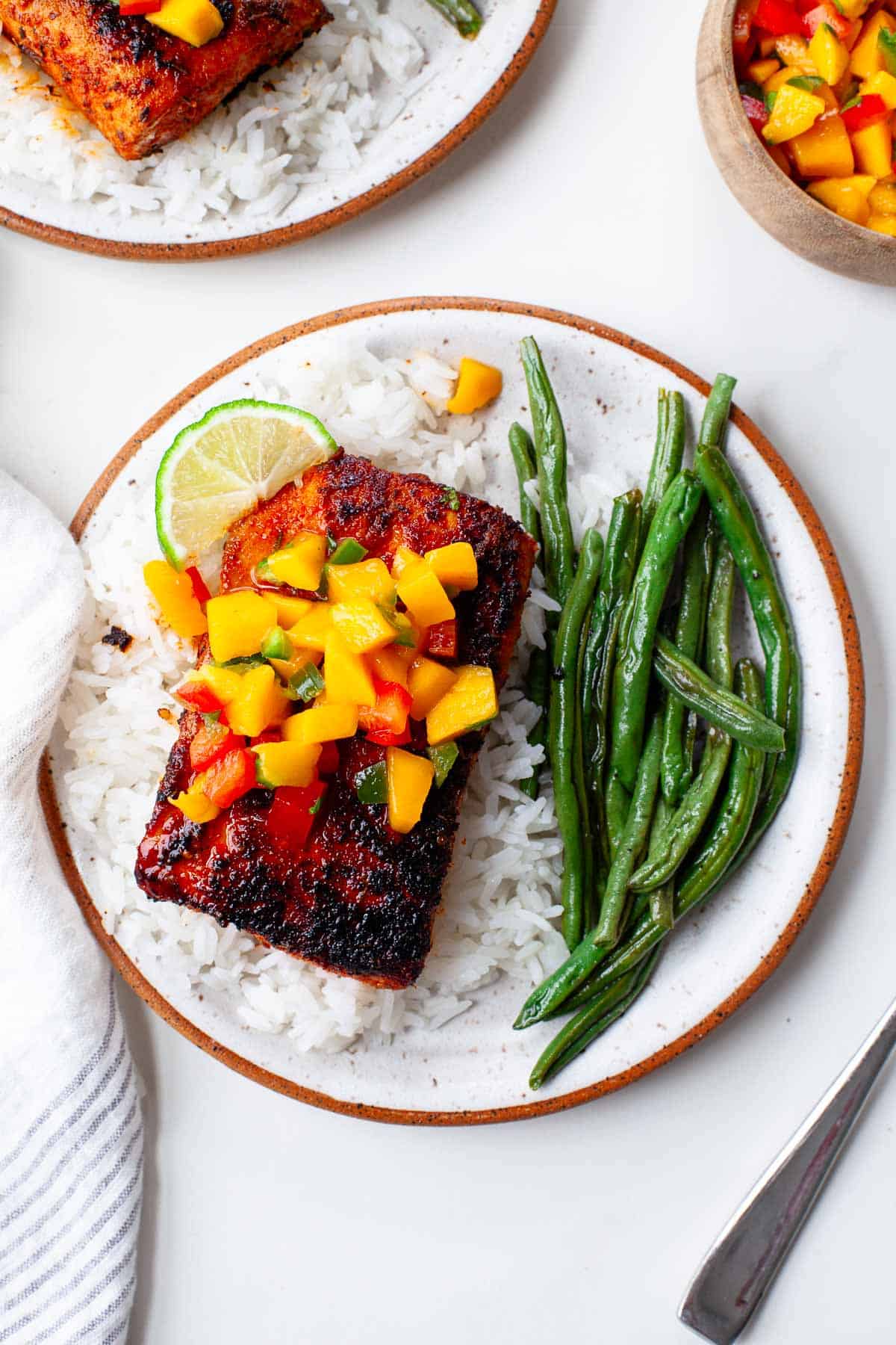 blackened mahi mahi atop a bed of white rice, garnished with fresh mango salsa and served with a side of green beans